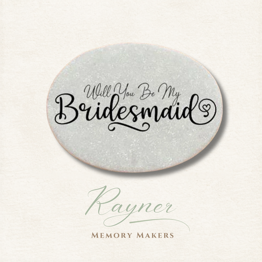 Oval pebble with 'Will You Be My Bridesmaid' text on a light gray background