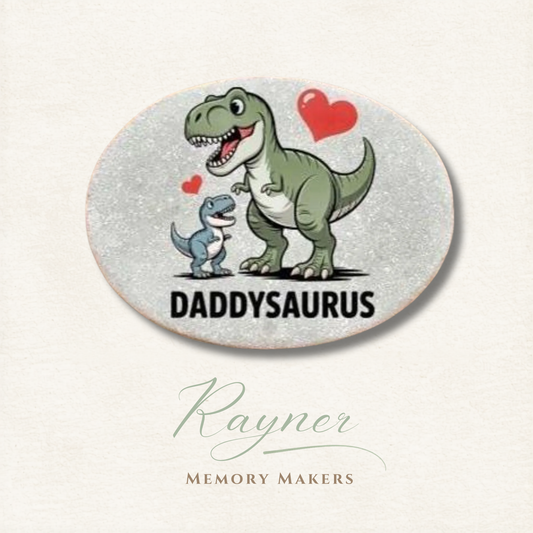 Oval coaster with cartoon dinosaurs and 'Daddysaurus' text on a light background, featuring the brand 'Rayner Memory Makers'.
