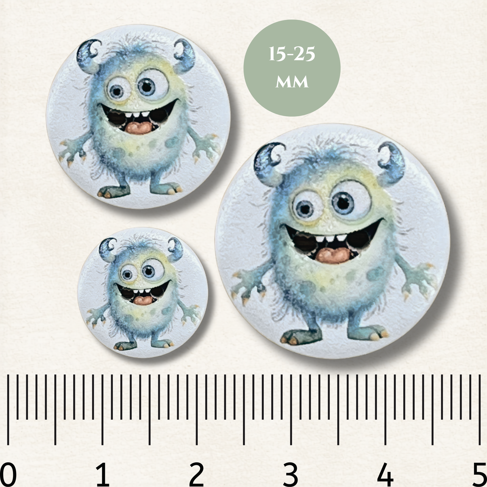 Three circular buttons with cartoon monster design and a ruler for size reference on a white background.