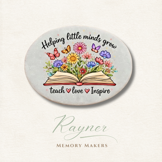 Round ceramic coaster with colorful flowers, book, and text 'Helping little minds grow, teach love inspire' on a light background.